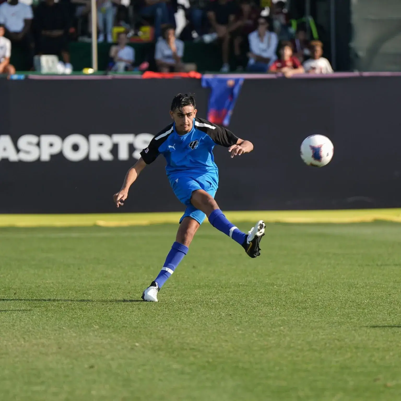 A man kicking a soccer ball on a grass field | Mina Cup 2024.