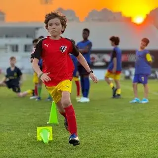 A young boy in red running on the field with a soccer ball.