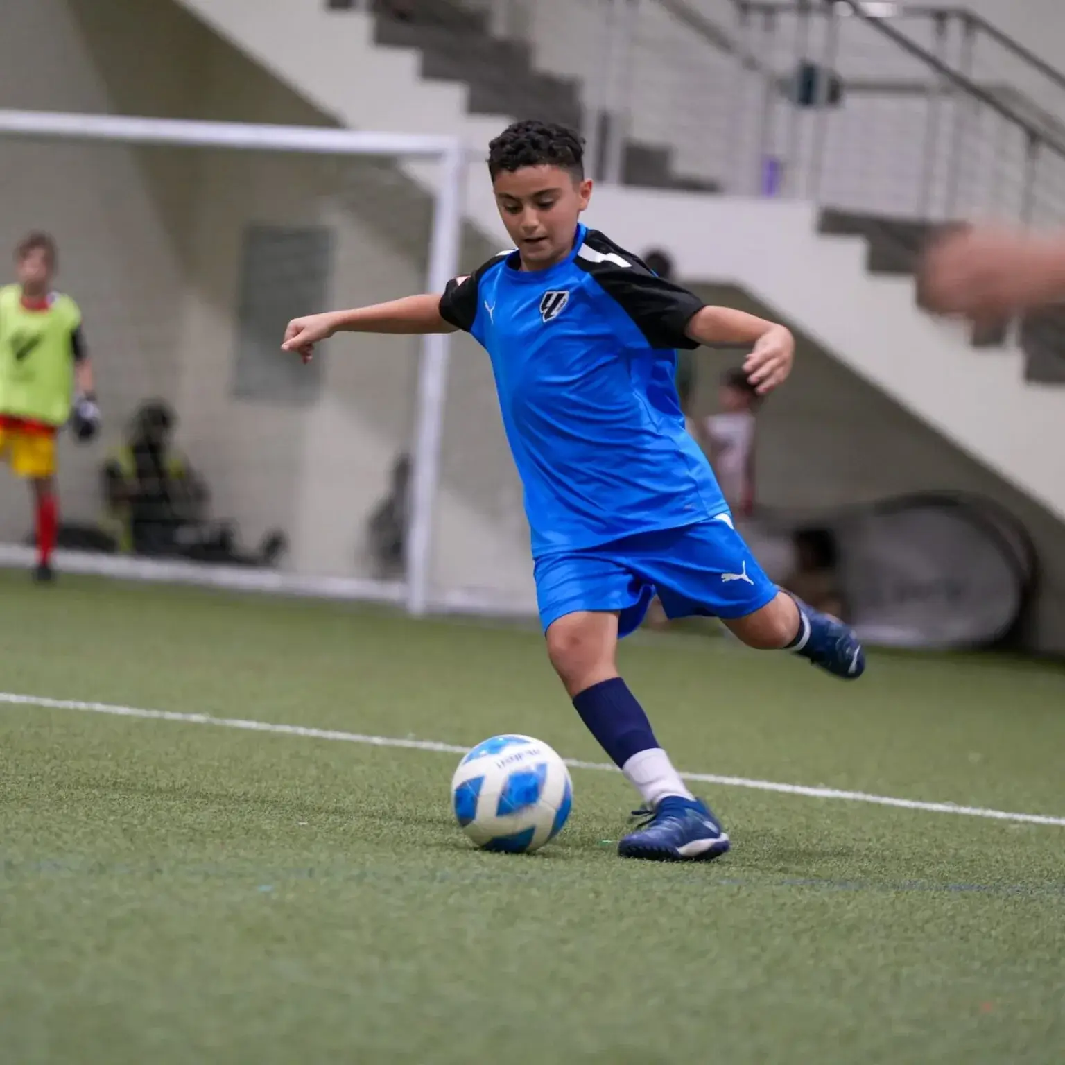 A young boy playing DOFA Season 2023 football on a field, kicking a ball with determination