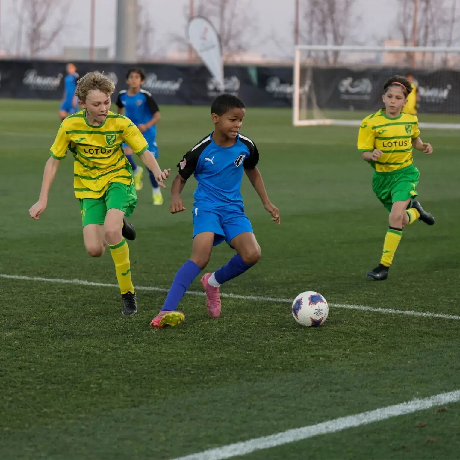 Group of kids enjoying a game of soccer on a green field at Mina Cup 2024.