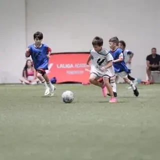 Kids Football Summer Camp |Kids playing soccer indoors on a field, having fun and kicking the ball around.