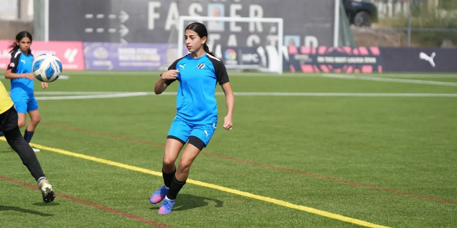 Two girls in blue uniforms playing soccer on a field DOFA Season 2023.