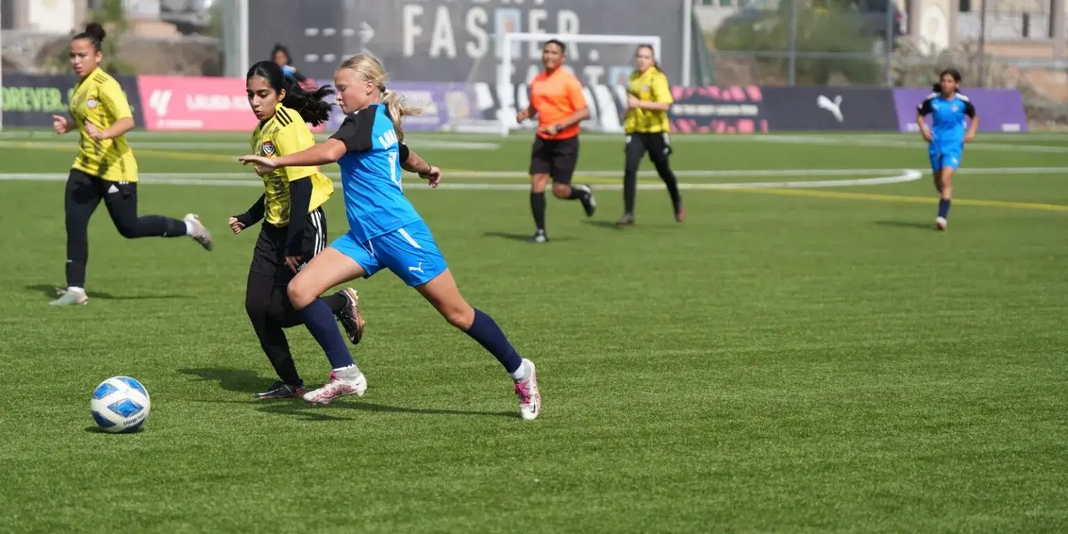 Women playing football on a field during a sunny day.