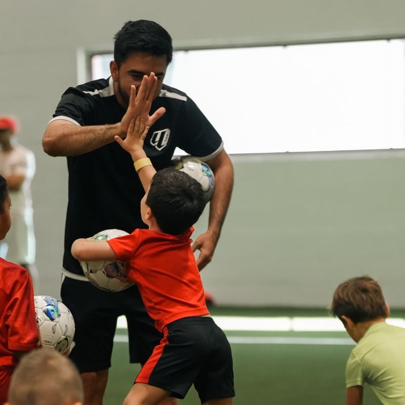 A young boy celebrating with a football coach at LaLiga Academy Dubai